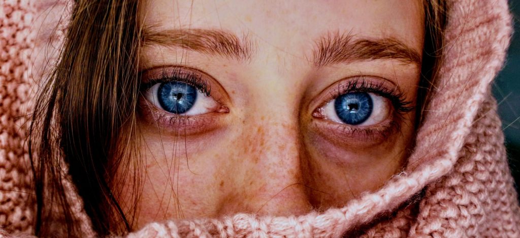 Intense close-up of a woman's blue eyes wrapped in a soft, pink knit scarf.