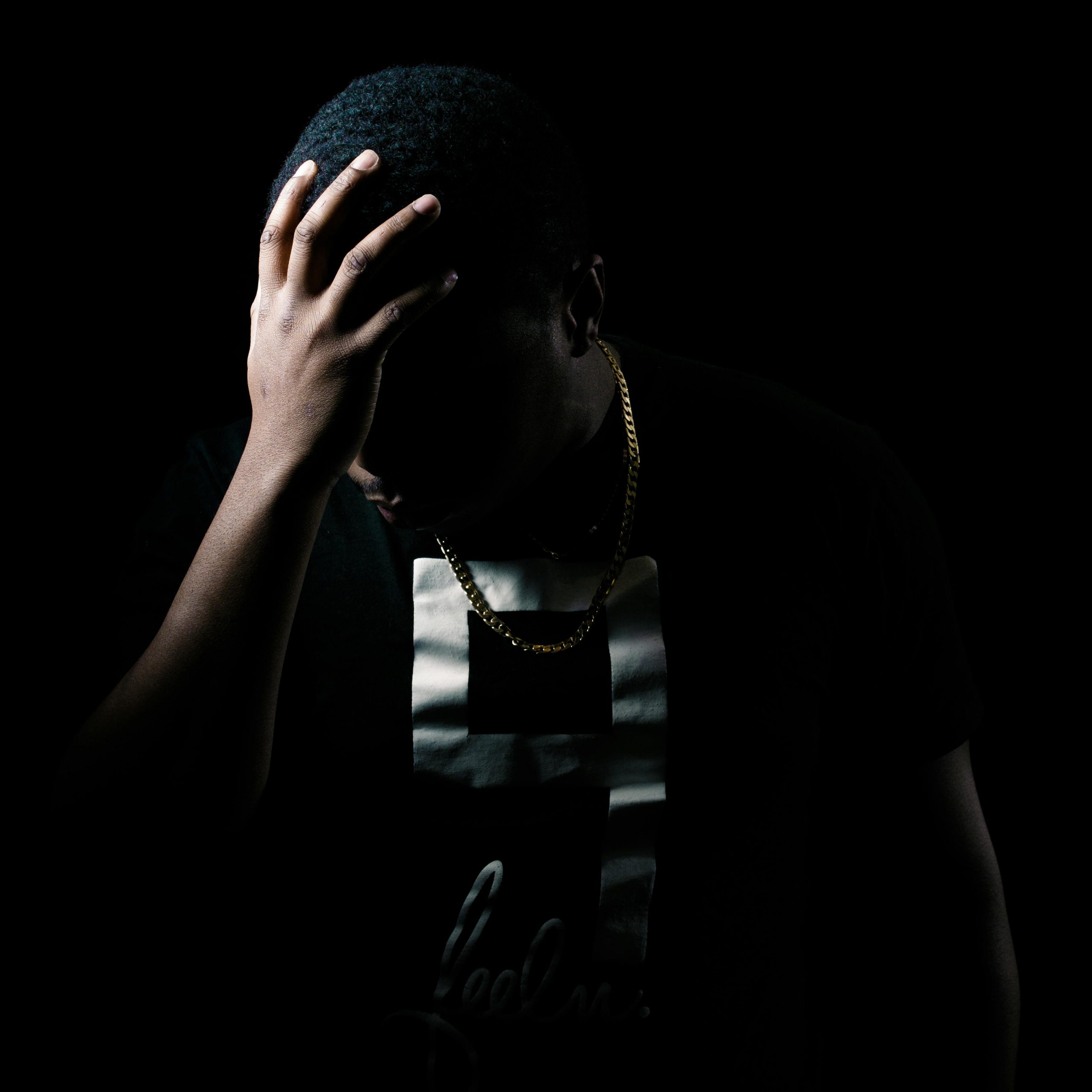 Silhouette of a man in thoughtful pose, hand on forehead, against black background.