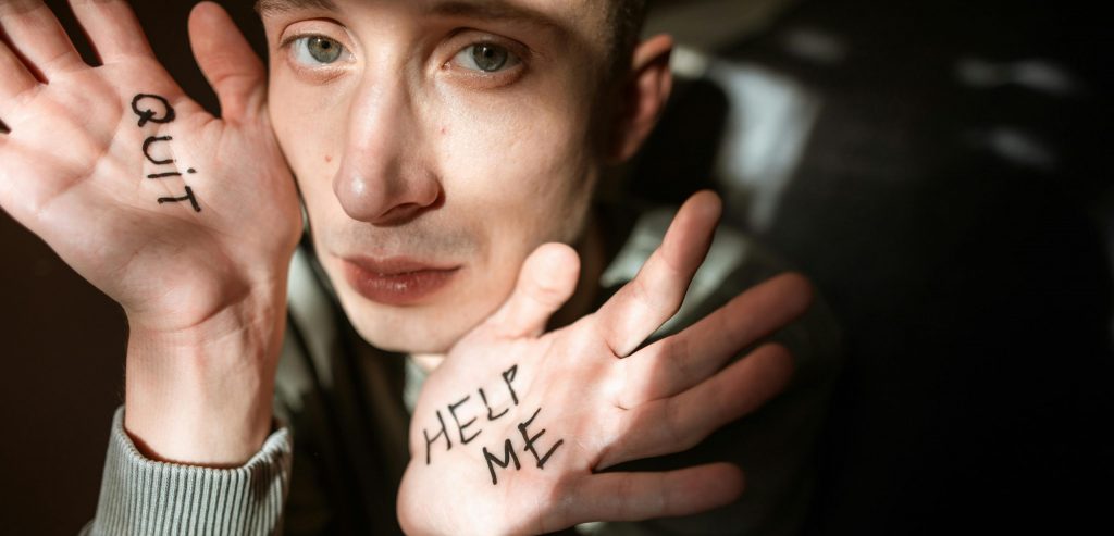 Close-up of a person showing palms with 'Help Me' and 'Quit' written, expressing emotions.