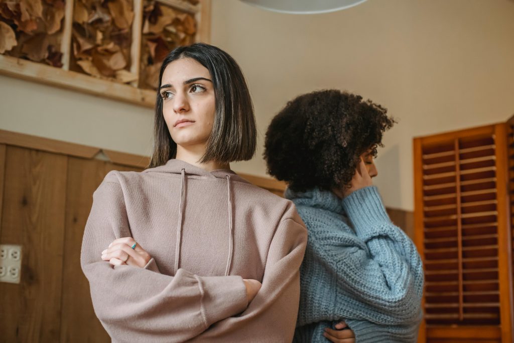 Two women facing away from each other, appearing upset in a home setting.