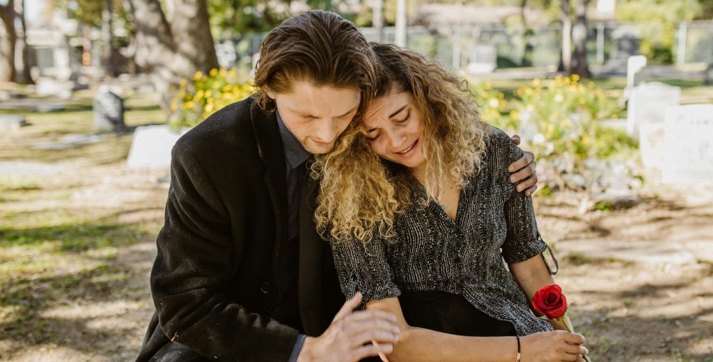 A comforting embrace in a serene graveyard captures grief and support.