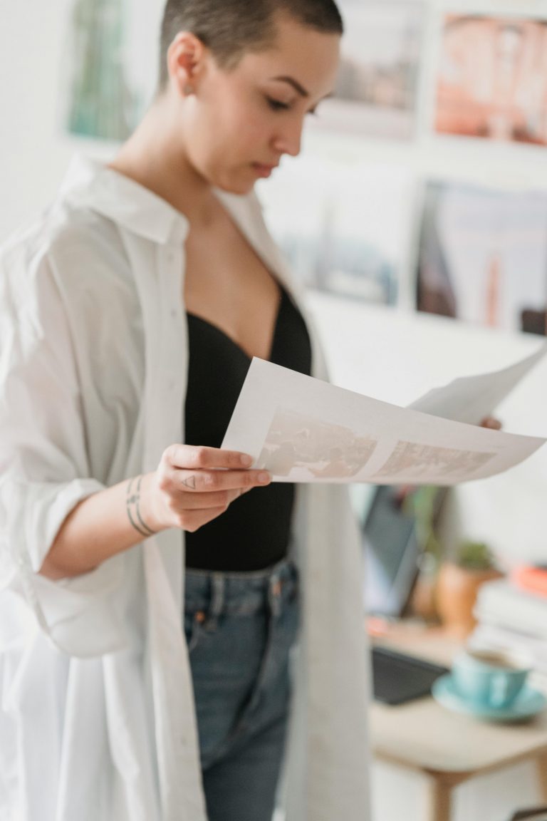 A woman in a casual outfit reviews documents in a bright home office setting.