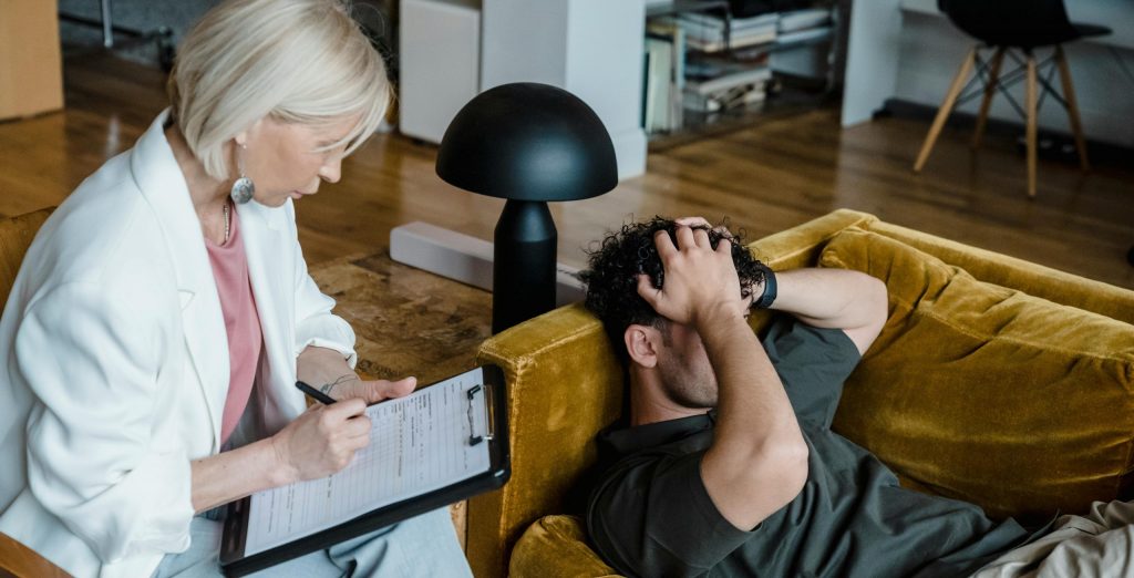 A therapist conducts a session with a client discussing mental health in a cozy office setting.